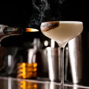 a hand holding a lighter and a cocktail glass