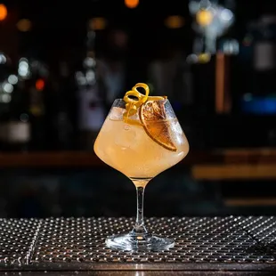 a cocktail in a glass with an orange garnish