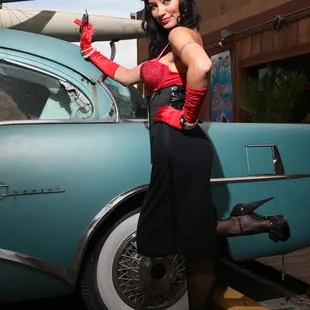 a woman in a red corset posing next to an old car