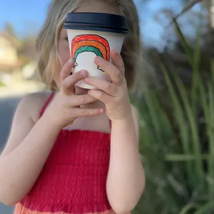 Kiddo in rainbow dress holding her perfect cinnamon streamed milk from Seven Seas!