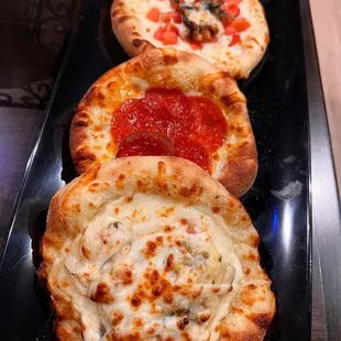 three small pizzas on a black plate