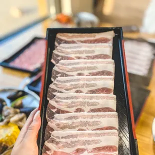 a person holding a tray of bacon