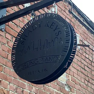 a black sign hanging from the side of a brick building