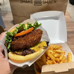 a hand holding a chicken sandwich and macaroni and cheese fries