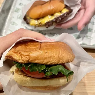 a person holding a hamburger and a sandwich