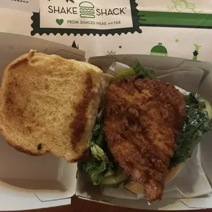 A small piece of fried chicken breast on a small bun with greasy wilted lettuce.