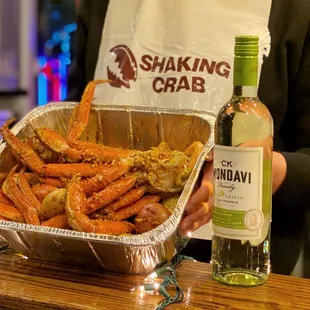a person holding a tray of crab legs and a bottle of wine