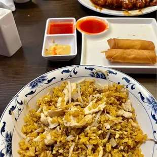 a plate of fried rice with chicken and spring rolls