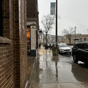 a wet sidewalk with cars parked on it