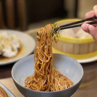 a person holding chopsticks over a bowl of noodles