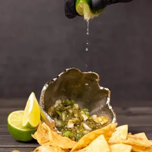 a hand squeezing a lime into a bowl of tortilla chips