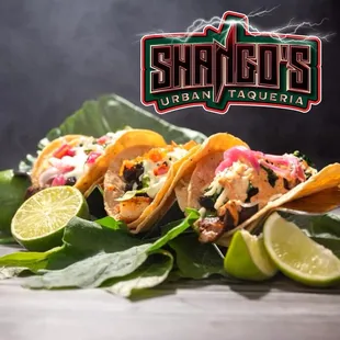 three tacos on a table with lime wedges