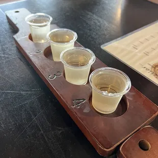 four shot glasses of white wine on a wooden tray