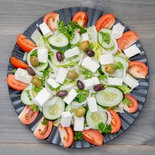 a plate of salad with tomatoes, cucumbers, olives, and feta cheese