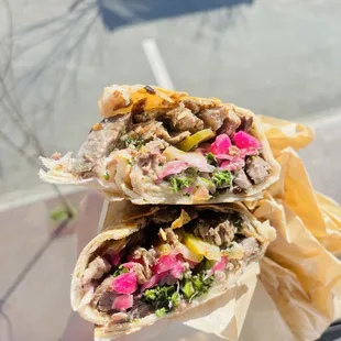 a hand holding a wrap of meat and vegetables