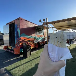 a person holding a burrito in front of a food truck