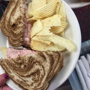 a person holding a plate with a sandwich and chips