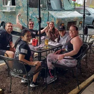 a group of people sitting at a table under an umbrella