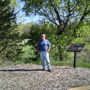 Dale Cox, son of Bill &amp; Margaret, standing between their benches at the tip of Clitty Lake.