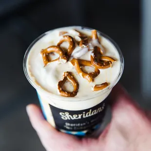 a hand holding a cup of ice cream and pretzels