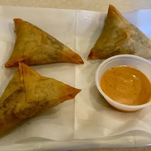 three triangular pastries and a small bowl of sauce