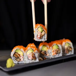 a person holding chopsticks over a plate of sushi