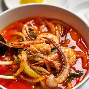 a bowl of seafood soup with chopsticks