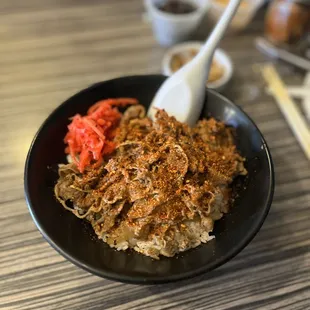 shows a bowl of ramen with a spoon and chopsticks