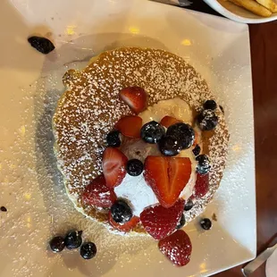 a pancake with strawberries, blueberries, and powdered sugar