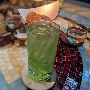 a glass of green drink on a mosaic table