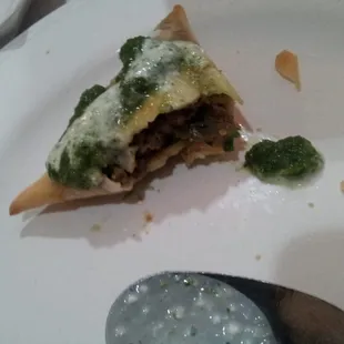 Meat Samosa with a view of its stuffing.  Topped with chutney &amp; yogurt.