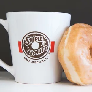 a glazed donut next to a coffee mug