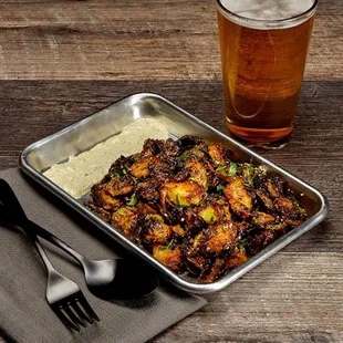 a tray of chicken wings with mashed potatoes and a glass of beer