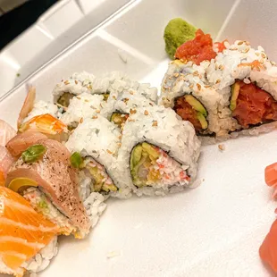 a variety of sushi rolls in a styrofoam container