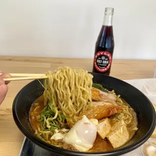 a person holding chopsticks over a bowl of ramen