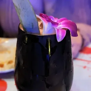a drink in a black glass with a flower in it