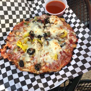 Individual veggie pizza with a side of hot sauce