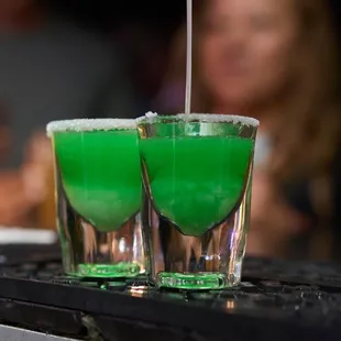 two glasses of green liquid with a straw