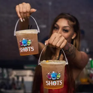 a woman holding two buckets of shots