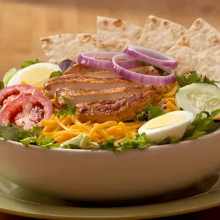 a salad with meat, cheese, tomatoes, cucumbers, and onions