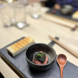 a bowl of food on a slate plate with a wooden spoon