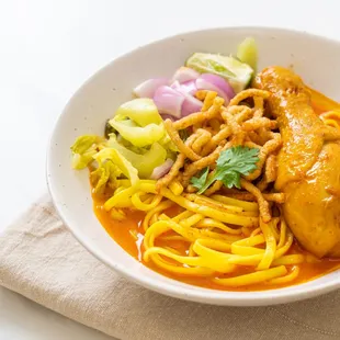 Northern Thailand yellow curry with crispy &amp; soft egg noodles, chicken leg, and thigh, with red onion, pickle mustard, beansprout, fresh lim