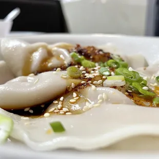 a plate of dumplings with sesame seeds and scallions
