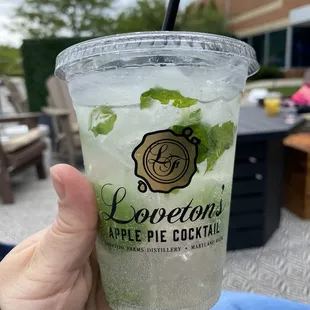 a hand holding a cup of loveton's apple pie cocktail
