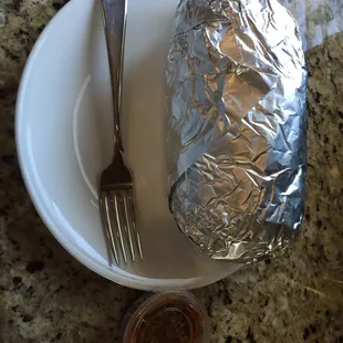 a foil wrapped potato on a plate with a fork