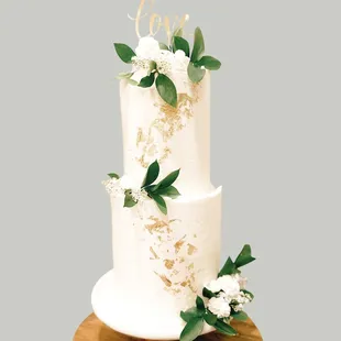 Wedding cake with white flowers, greenery, and gold leaf