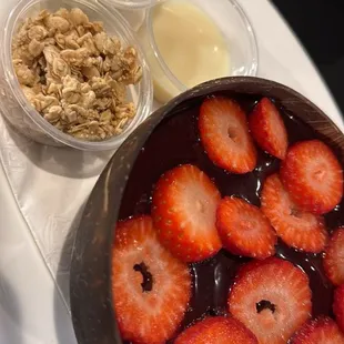 Açaí bowl topped with strawberries -- sweet powdered milk, condensed milk, and granola condiments.
