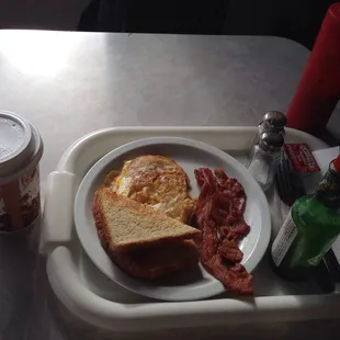 a breakfast tray with a sandwich, bacon, and coffee