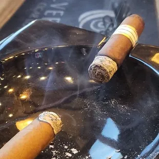 two cigars on a black ashtray