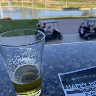 a glass of beer on a table with a golf course in the background